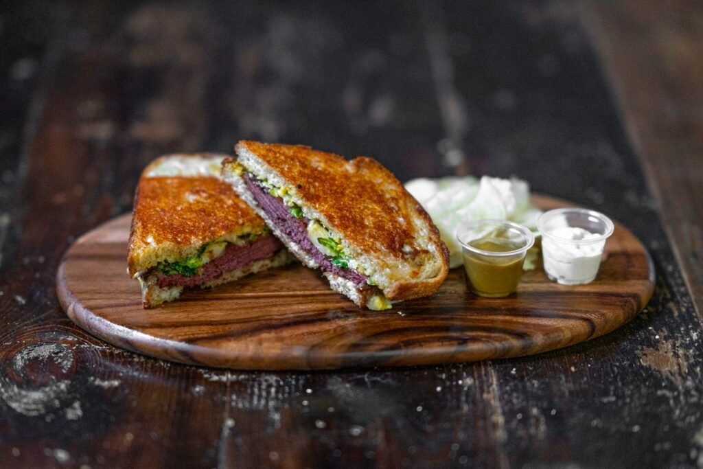Close-up of a grilled sandwich with sauces on a wooden board, showcasing a rustic meal.