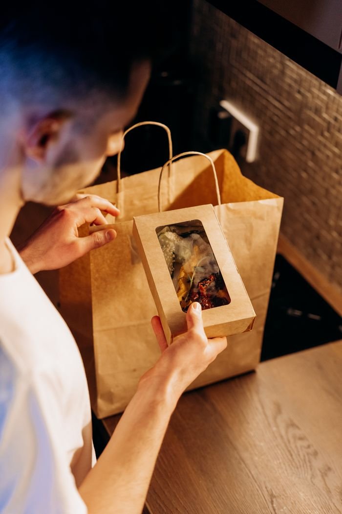 A man at home is unpacking a food delivery from a paper bag on a kitchen counter.