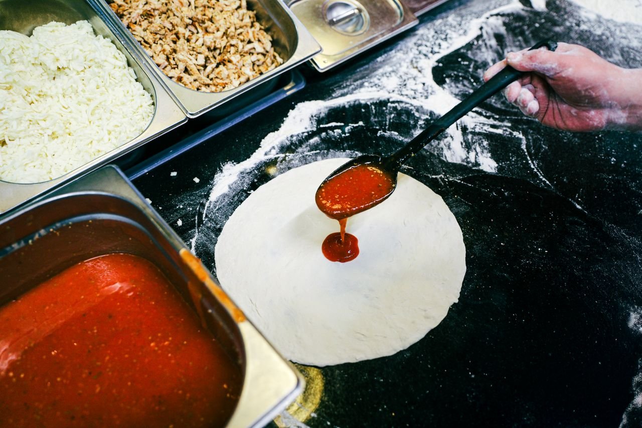Preparing fresh pizza dough with tomato sauce, cheese, and meat toppings, perfect for culinary themes.